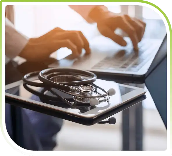 Healthcare professional using a laptop with a stethoscope placed on a tablet