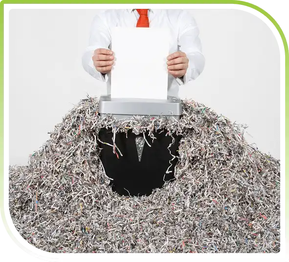 Person shredding documents using paper shredding machine with shredded papers on table for secure document disposal